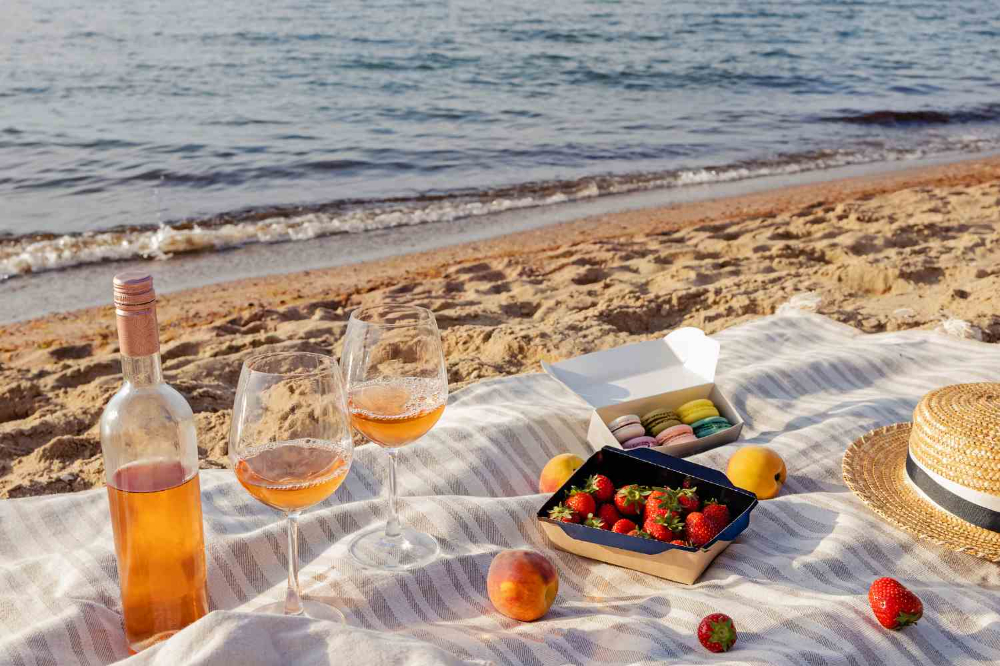 Beachside picnic setup with ros wine and macarons, showcasing relaxing tailgating wines for summer events